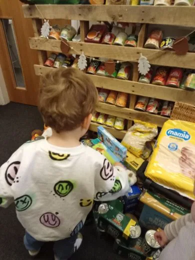 A small child reaching towards pallet shelves stacked with tins and food donations